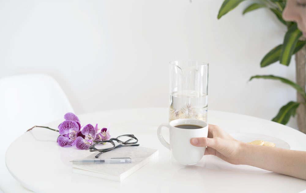 Hand holding coffee with eyeglasses on table