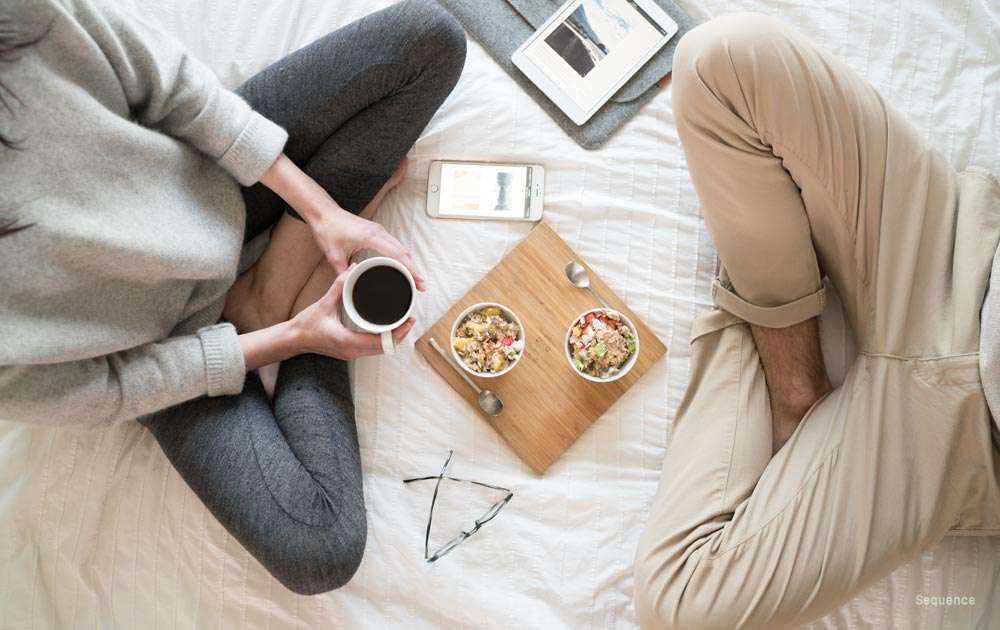 An overhead view of two people sitting on a bed having brunch