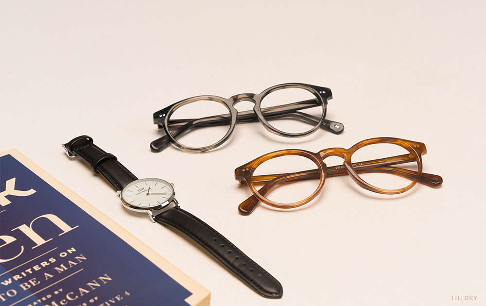Two pairs or glasses frames next to a watch and a book