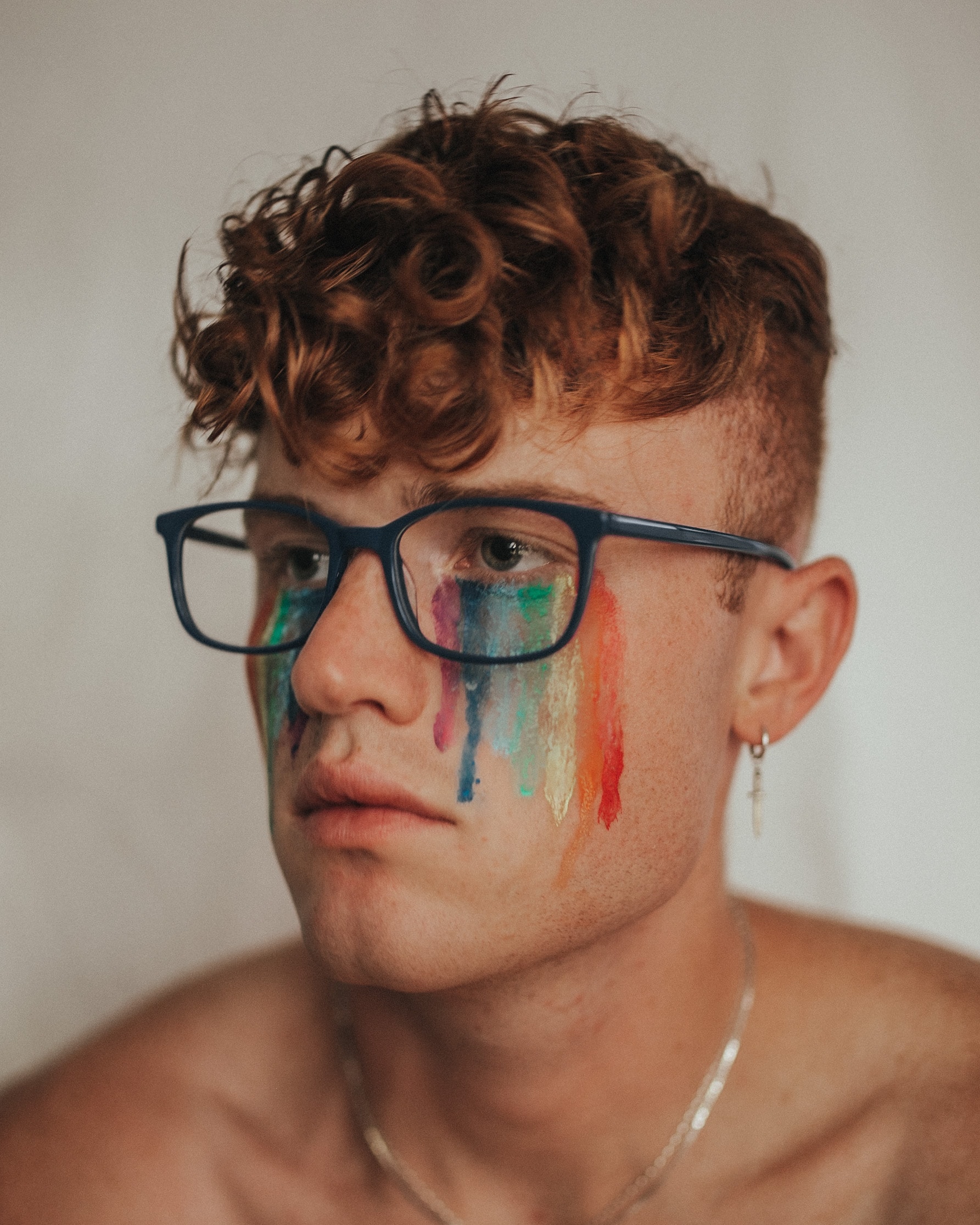 A person wearing glasses with rainbow paint on their face