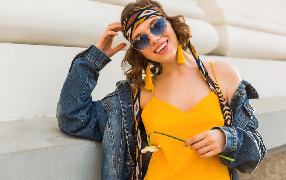 A smiling woman wearing a yellow dress and blue lens sunglasses