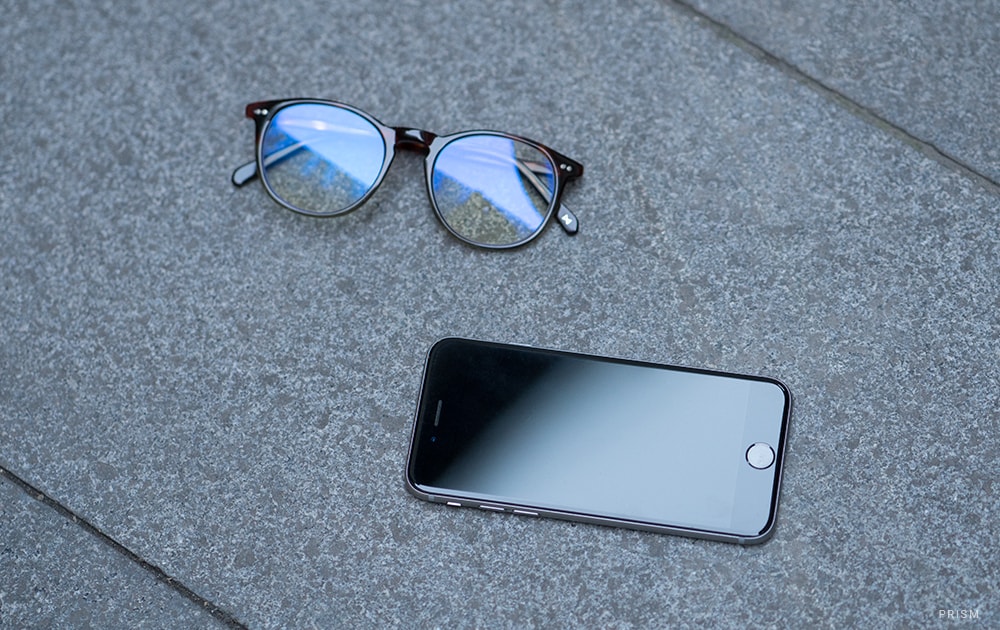 A pair of blue light blocking glasses next to a smartphone