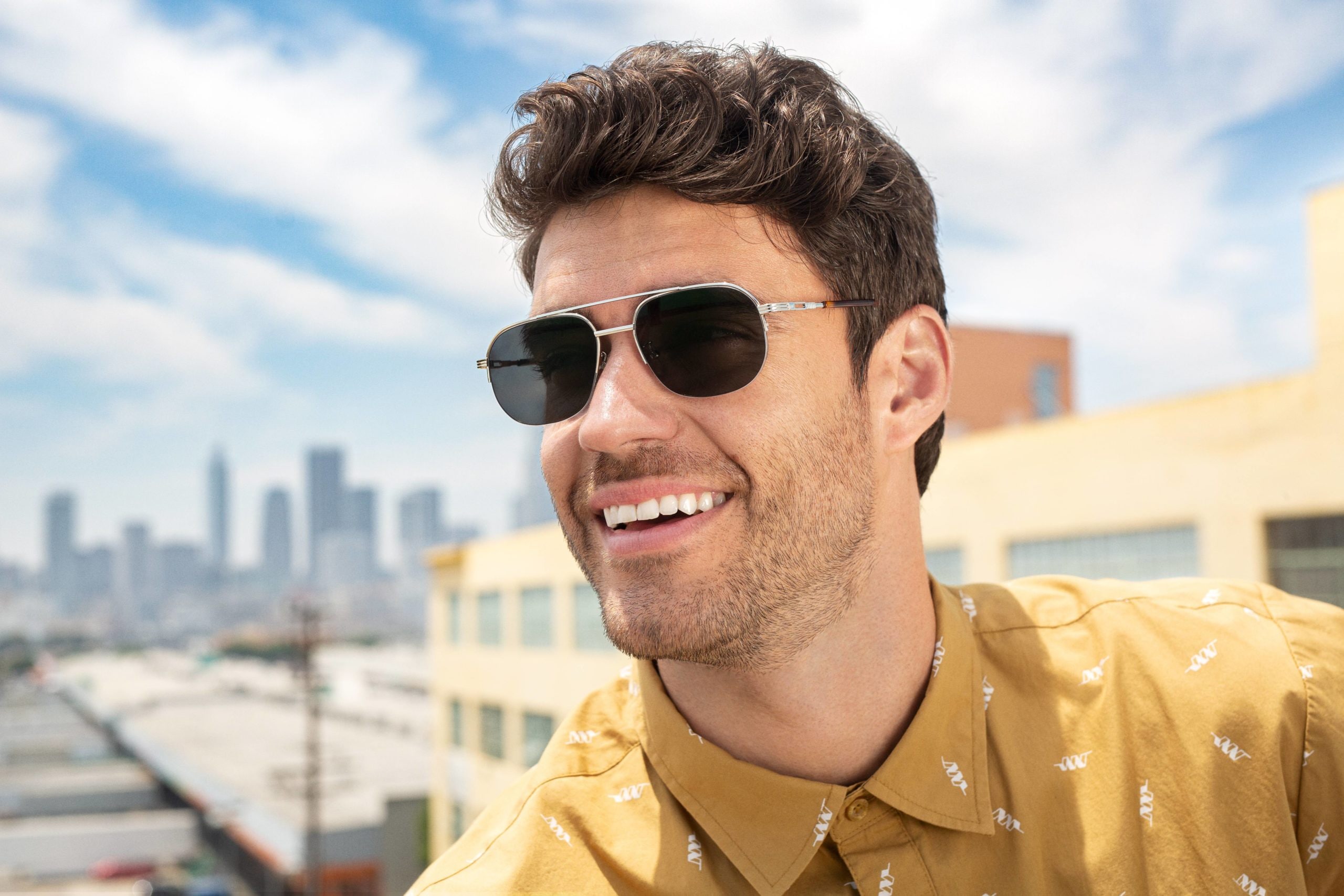 A man wearing prescription sunglasses with a city in the background
