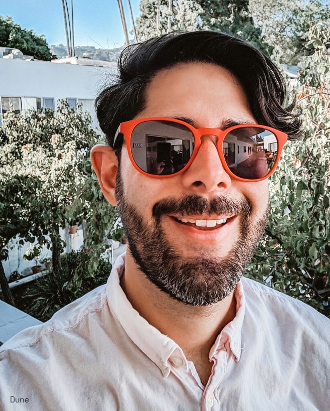 A man smiling wearing crimson eyeglasses