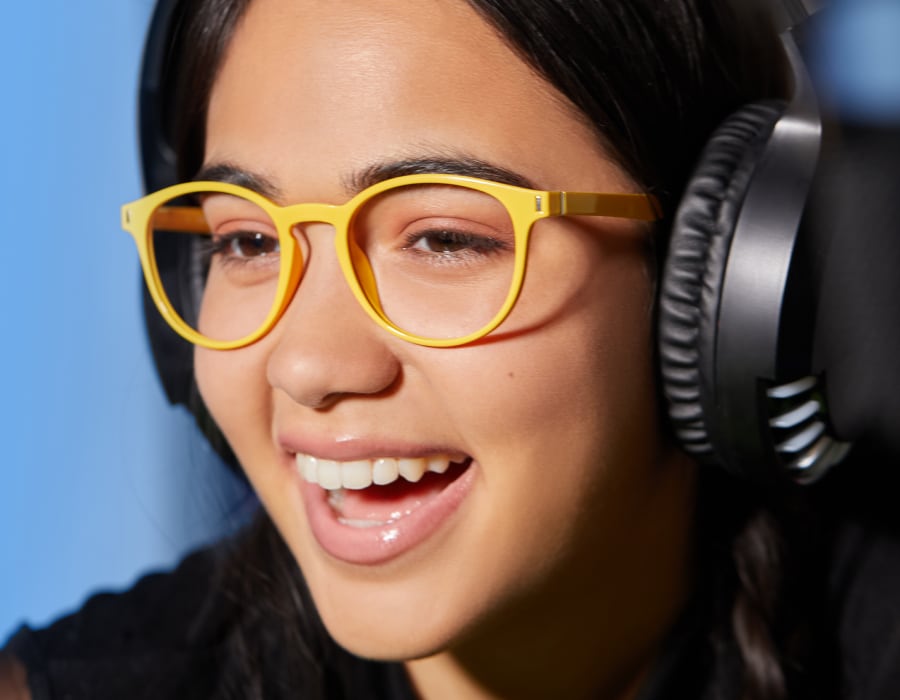 A laughing woman wearing gaming glasses and headphones