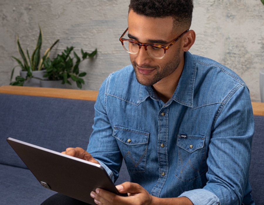 A man in a blue shirt and gaming glasses using a laptop