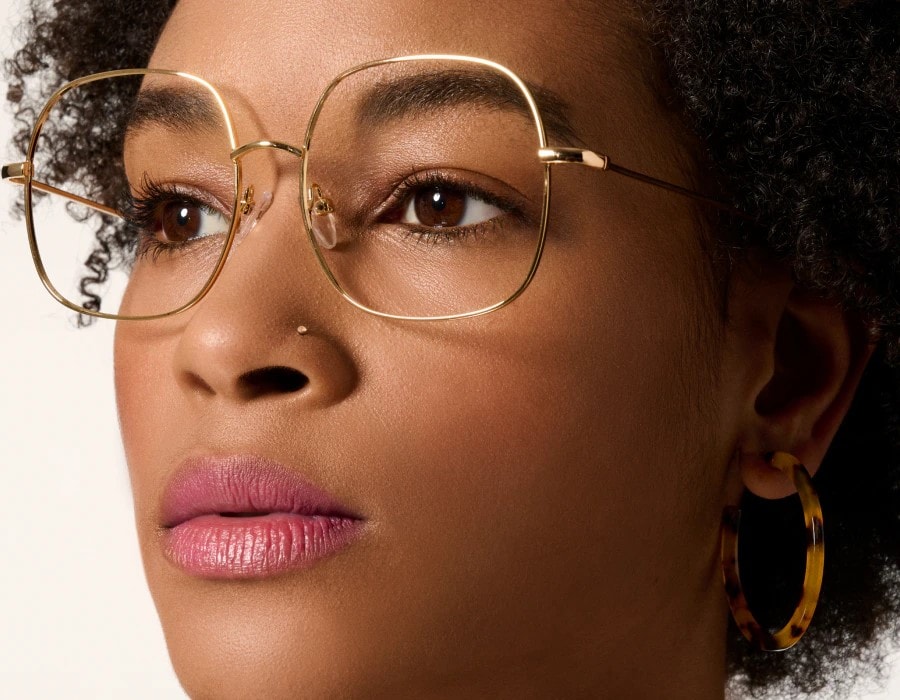 A closeup of a woman's face looking to the left and wearing eyeglasses with gold colored frames