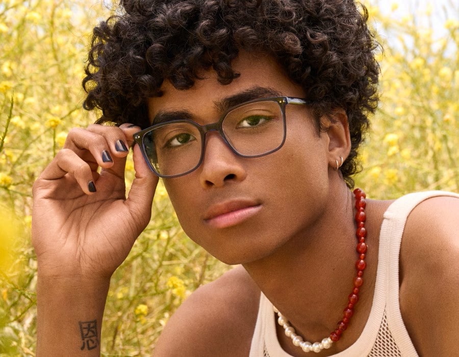 A young man in a field wearing square-shaped eyeglasses