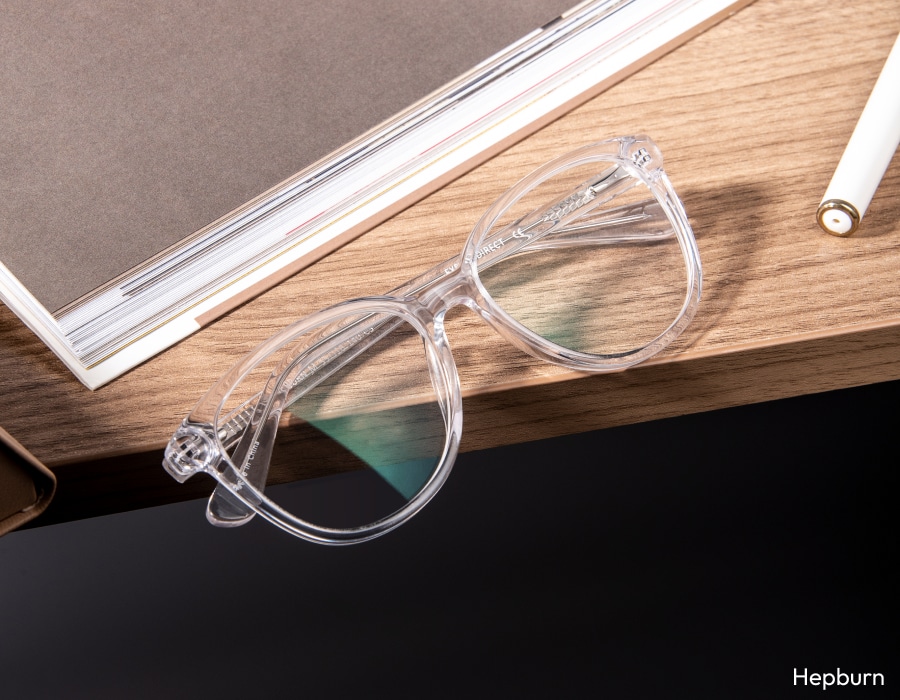 A pair of eyeglasses with clear frames hanging over the edge of a table
