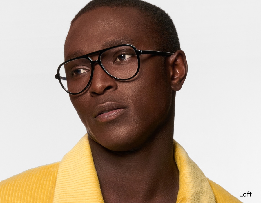 A man looking off camera wearing black eyeglasses with aviator-style frames