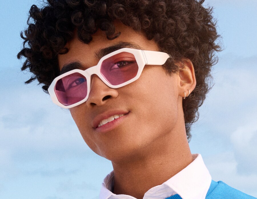 A boy wearing white frame sunglasses with pink-tinted lenses 