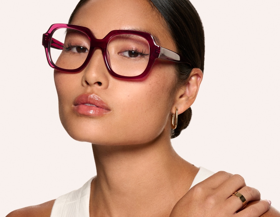 A woman with her hand on her shoulder wearing large eyeglasses with translucent red frames