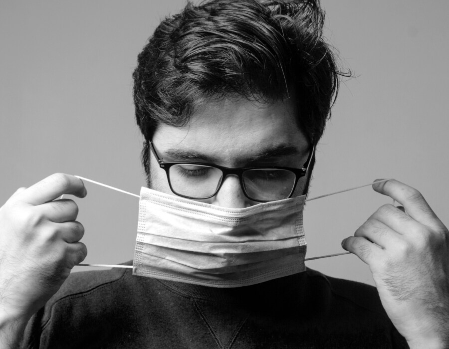 A man wearing eyeglasses putting on a face mask