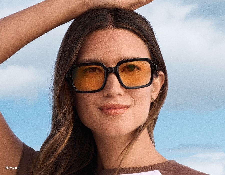 A woman with her hand on her heard wearing black frame sunglasses with amber-colored lenses