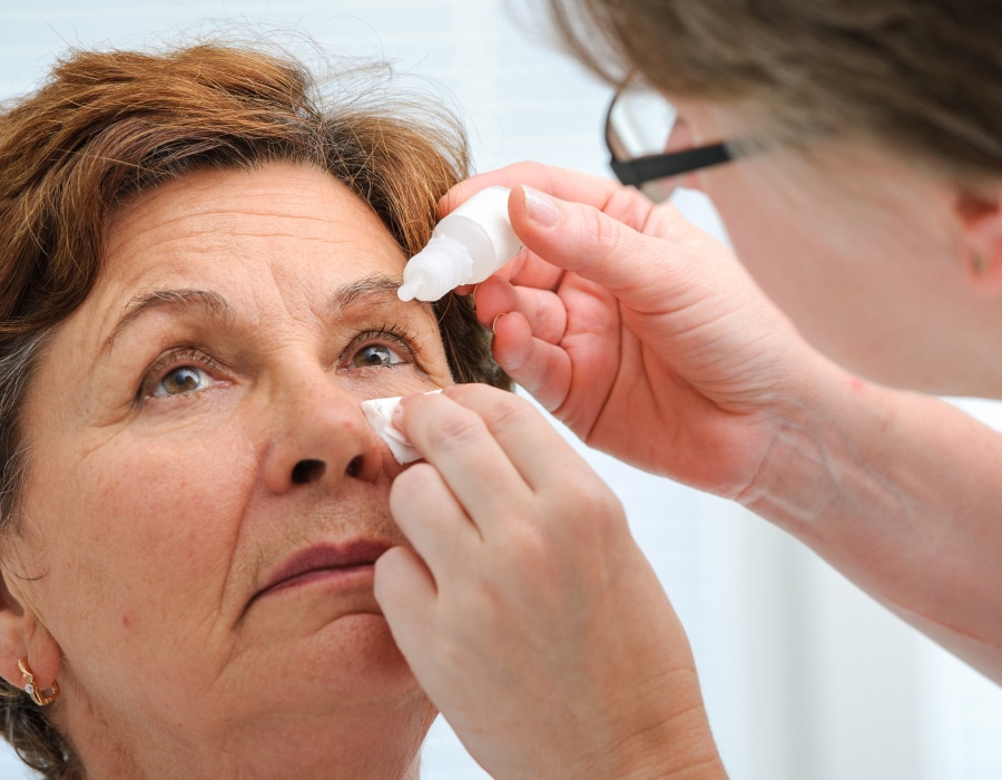 A medical professional applying eye drops to a patient's left eye