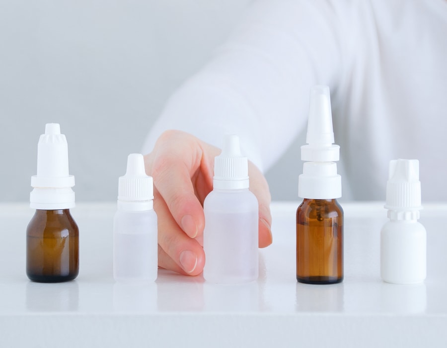 Four bottles of eye drops lined up on a table with a hand resting behind them