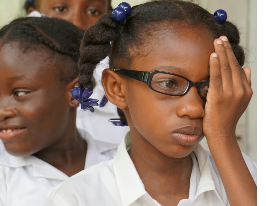 A girl wearing eyeglasses covering her left eye with her hand