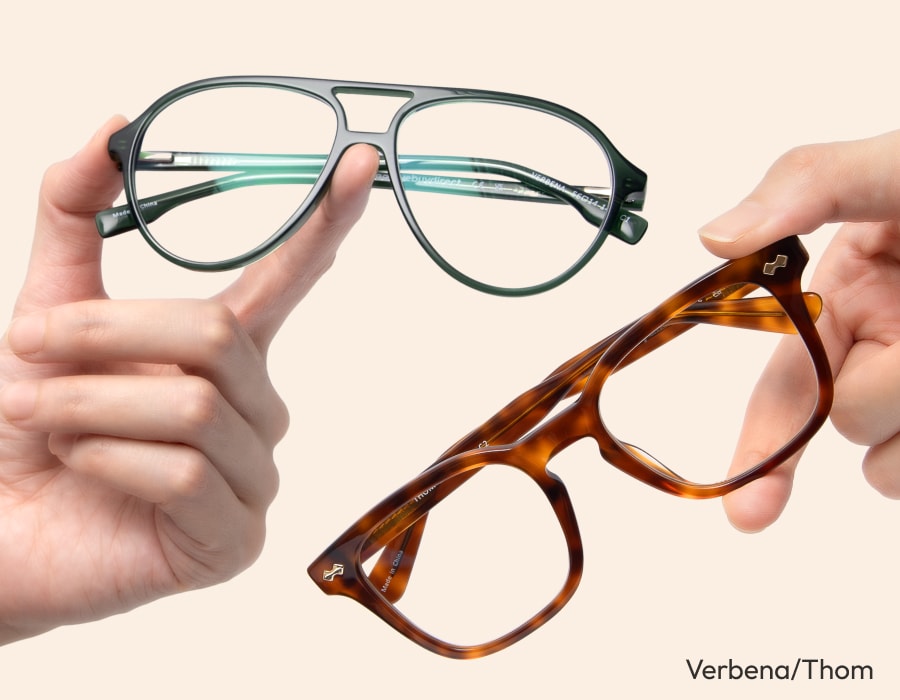 Hands holding two pairs of eyeglasses, one with a green frame and one tortoiseshell