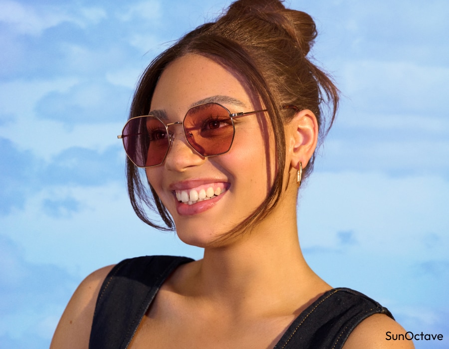 A woman in front of a blue sky wearing eyeglasses with brown-tinted lenses