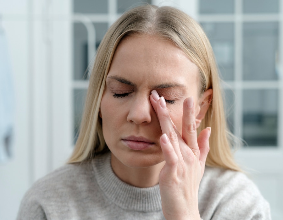 A woman in a gray sweater rubbing the inner corner of her left eye