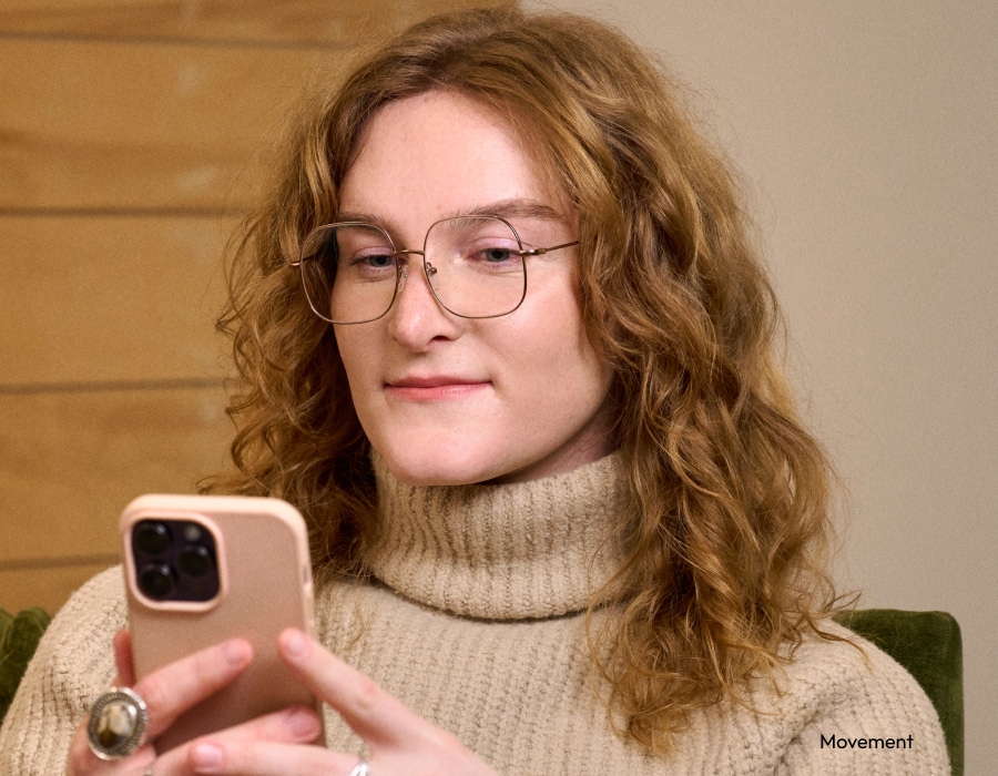 A woman in a turtleneck sweater wearing eyeglasses and looking at her phone
