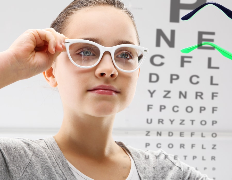 A girl wearing white eyeglasses next to a snellen eye chart