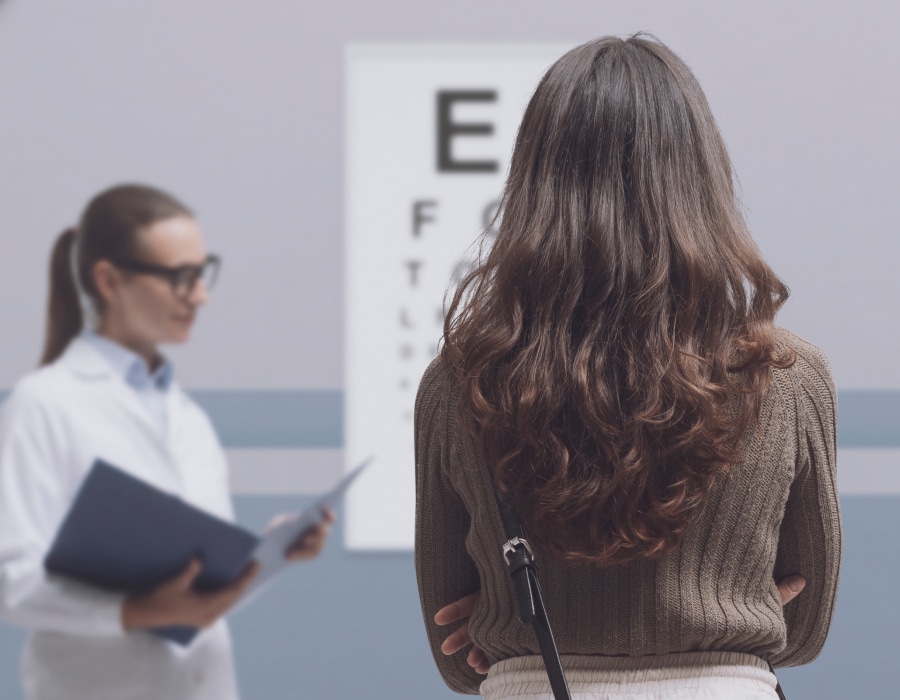 A woman standing in front of a snellen eye chart while an eyecare professional conducts an eye test