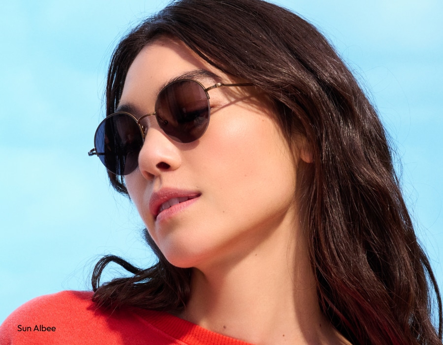 A woman in front of a blue sky wearing round sunglasses