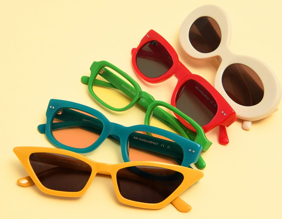 A selection of sunglasses with different colors and shapes on a yellow surface