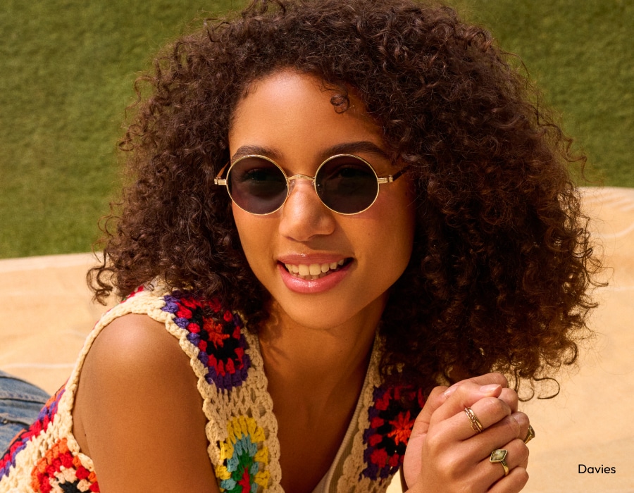 A woman lying in a field wearing round sunglasses