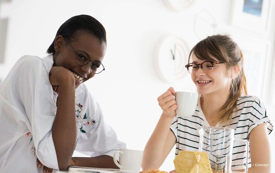Two women sitting at a table with a white background