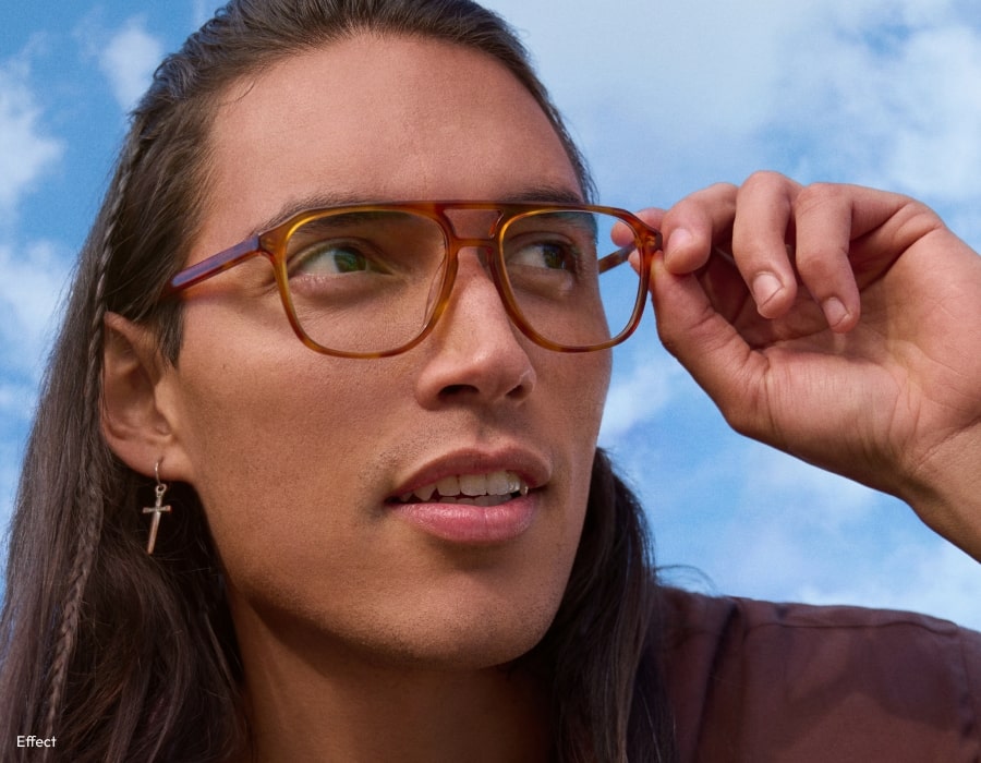 A man in front of a blue sky wearing large aviator style eyeglasses