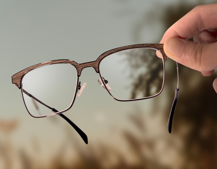 A hand holding a pair of browline-style eyeglasses with wood-texture frames