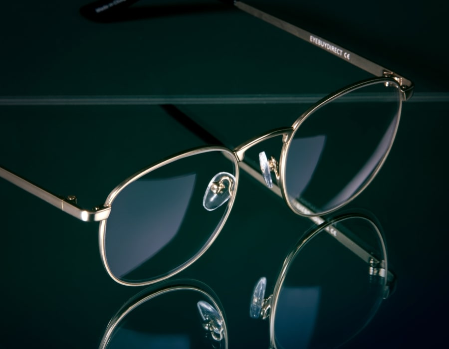 A pair of metallic eyeglasses with round frames on a black reflective background