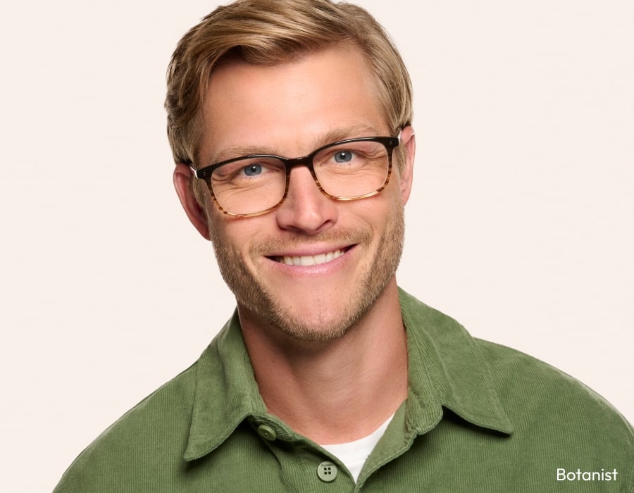 A man in a green shirt smiling wearing eyeglasses with striped-texture frames