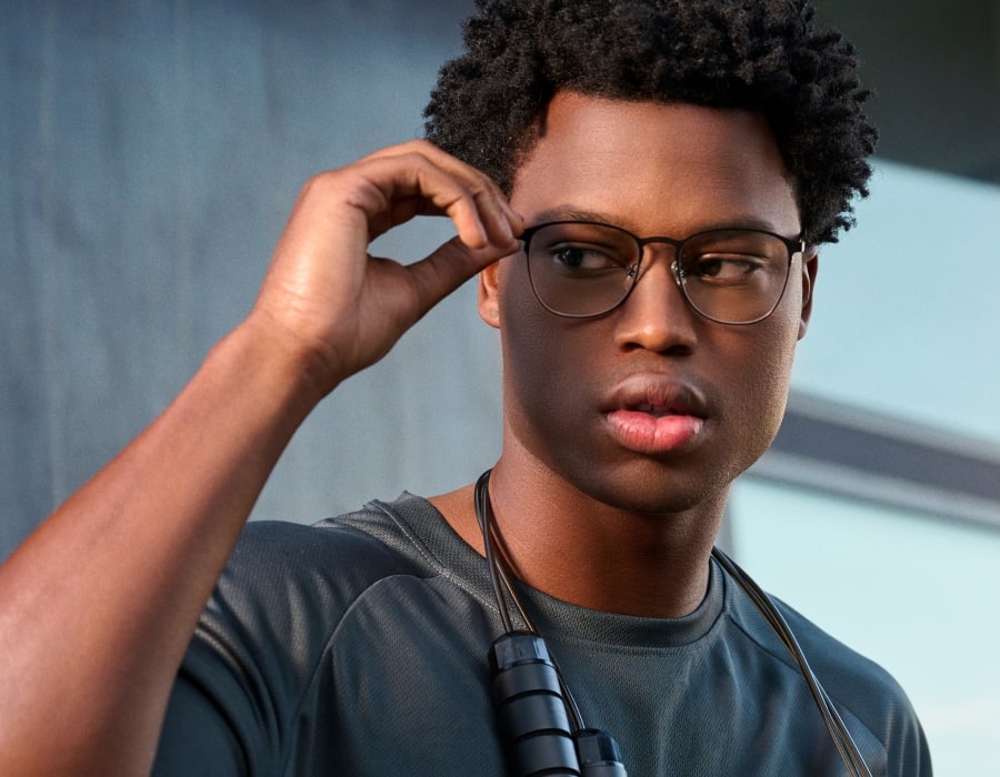 A man in front of a brushed concrete wall wearing round eyeglasses with thin, metallic rims