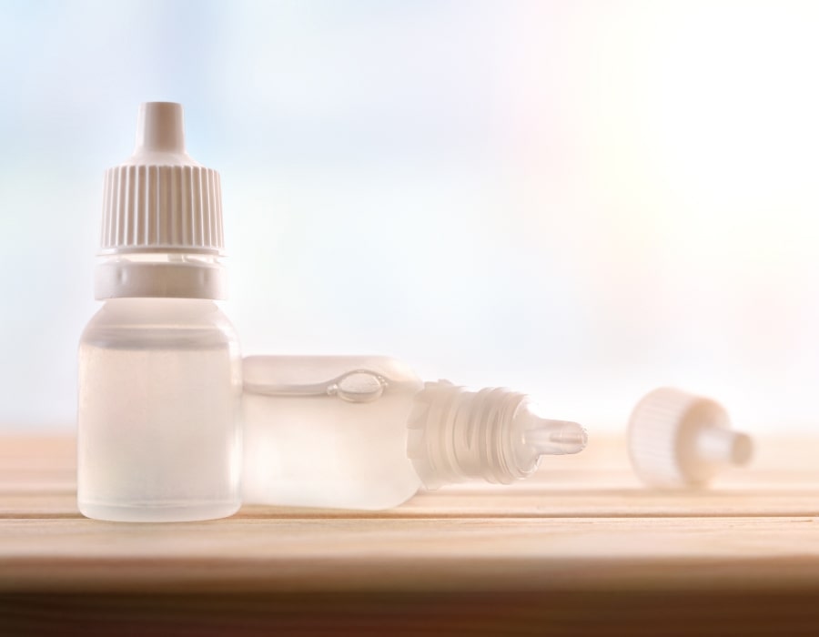 Two bottles of eye drops with tan caps, one lying on its side with the cap off