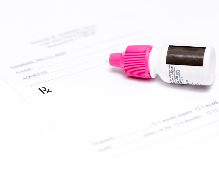 A bottle of eyedrops with a pink cap lying on a document