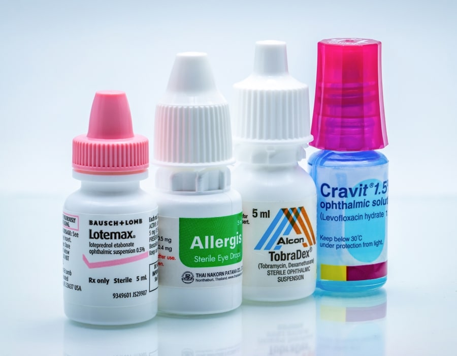 4 bottles of eye drops in a row, two with pink caps and two with white caps