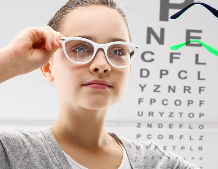 A girl wearing white eyeglasses next to a snellen eye chart