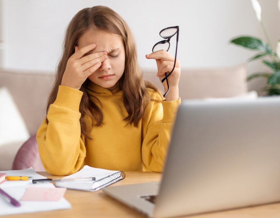 A girl holding her head sitting in front of a laptop