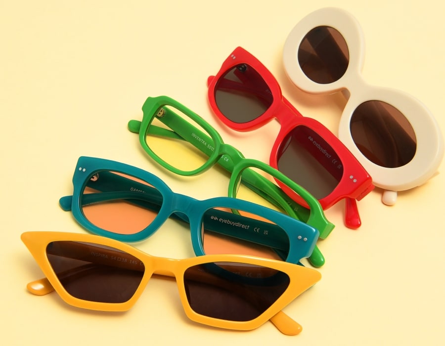 A selection of sunglasses with different colors and shapes on a yellow surface