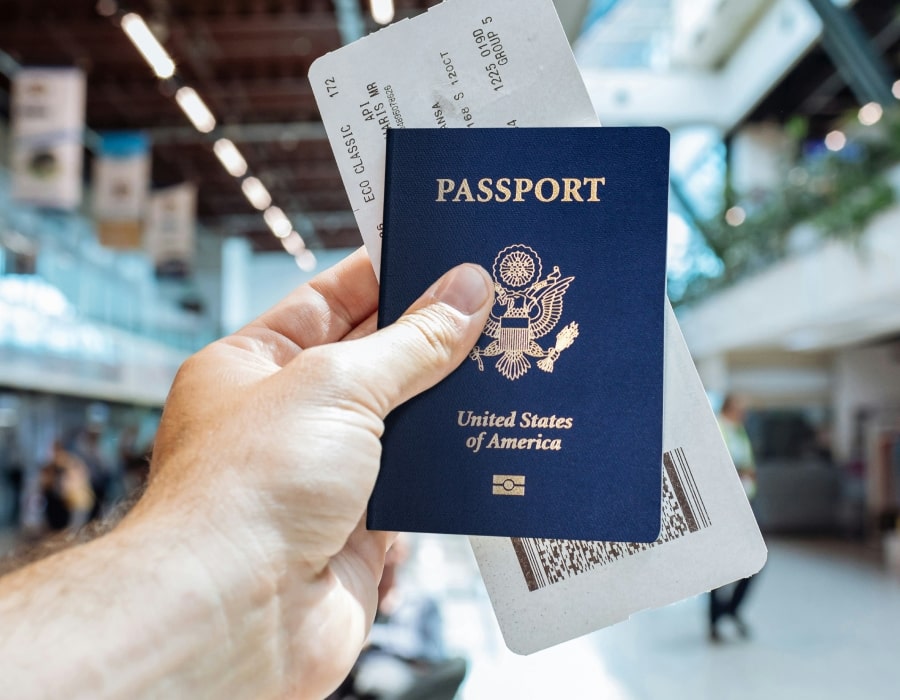 A hand holding a United States passport and a flight ticket