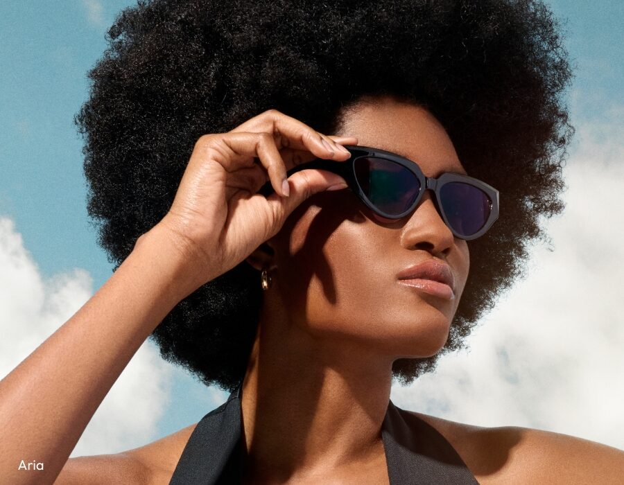 A woman adjusting her black cat-eye sunglasses in front of a blue sky background