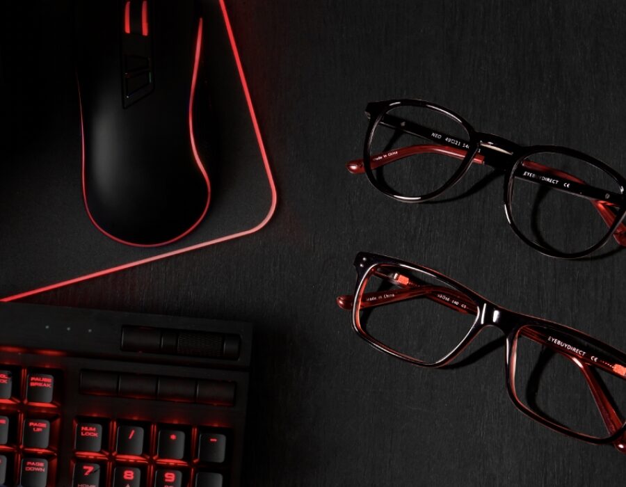 A pair of gaming glasses frames next to a gaming mouse and keyboard