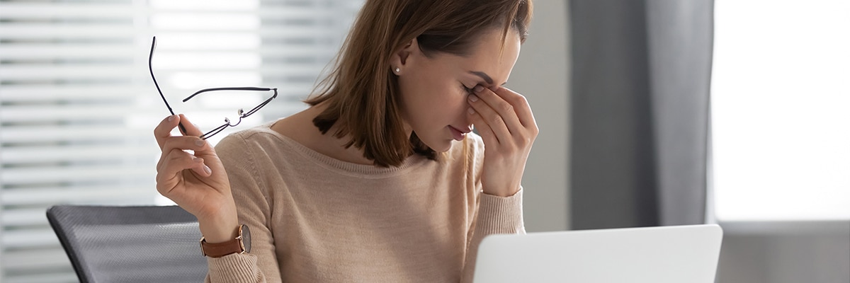 A woman using a laptop suffering from a headache