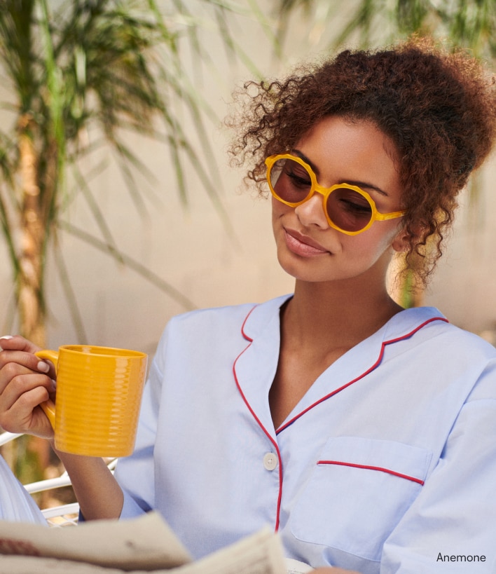 A woman holding a mug wearing reading sunglasses