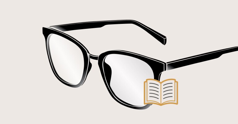 Une personne chauve et à la barbe grise porte des lunettes et sourit avec les dents, en regardant vers la caméra, un livre à la main.