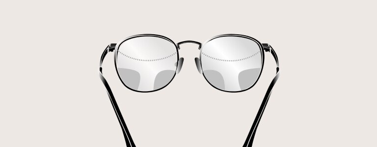 Une personne aux cheveux gris portant des lunettes et une chemise blanches regarde directement dans la caméra en souriant la bouche entrouverte.