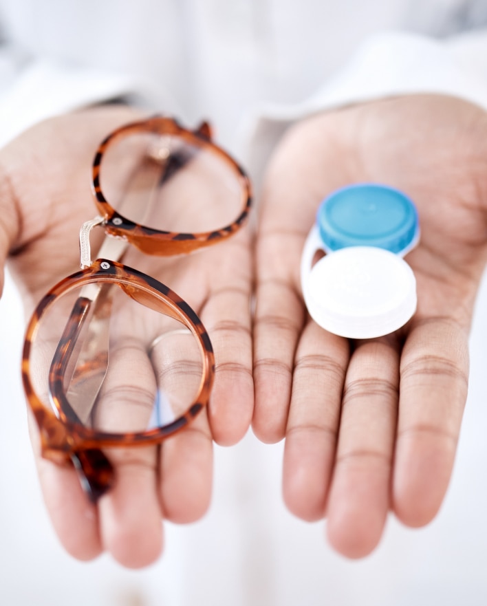 a doctors hands holding a pair of glasses in the right and a contact lens container in the left